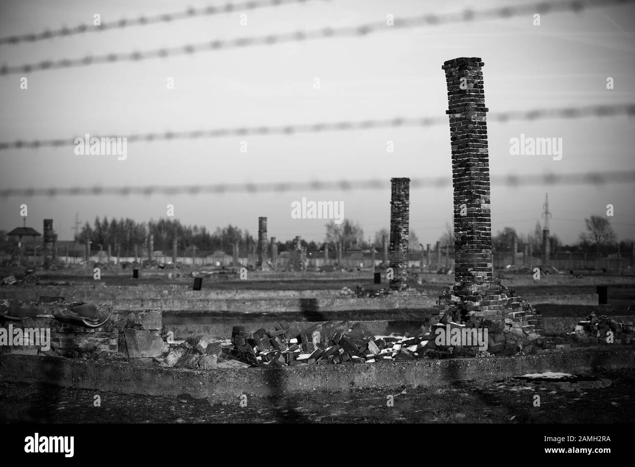 Auschwitz- Birkenau, Polen - Elektrozaun mit Stacheldraht, zerstörte Kasernen, Gaskammern und Ziegelsteinkrematoriumsschornsteine im Konzentrationslager Stockfoto