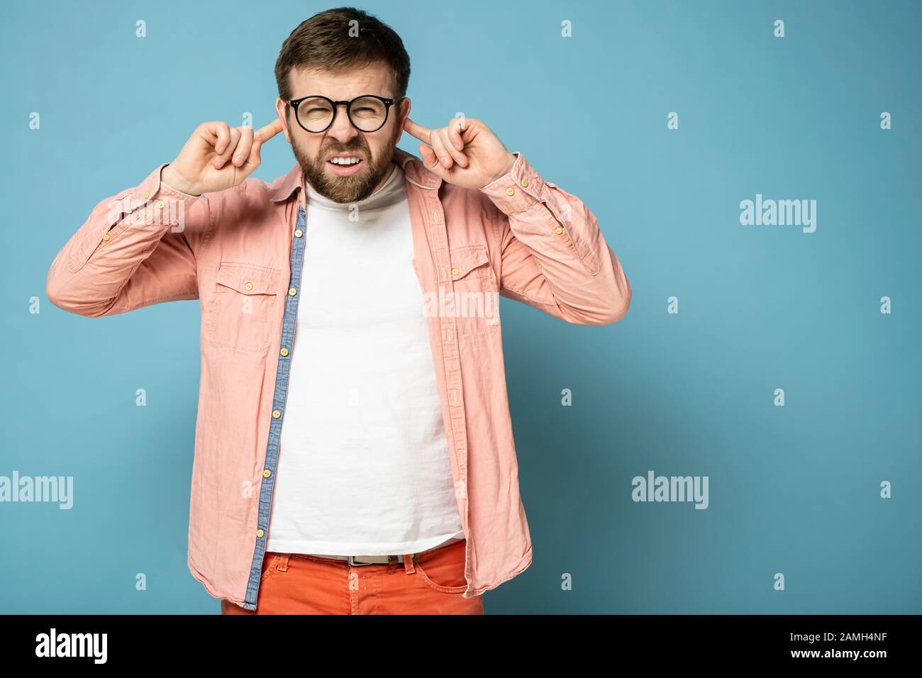 Seltsamer Mann mit einem lustigen Grimace drückt die Finger auf die Ohren und versucht etwas zu hören und sieht mit verengten Augen an der Kamera aus. Stockfoto