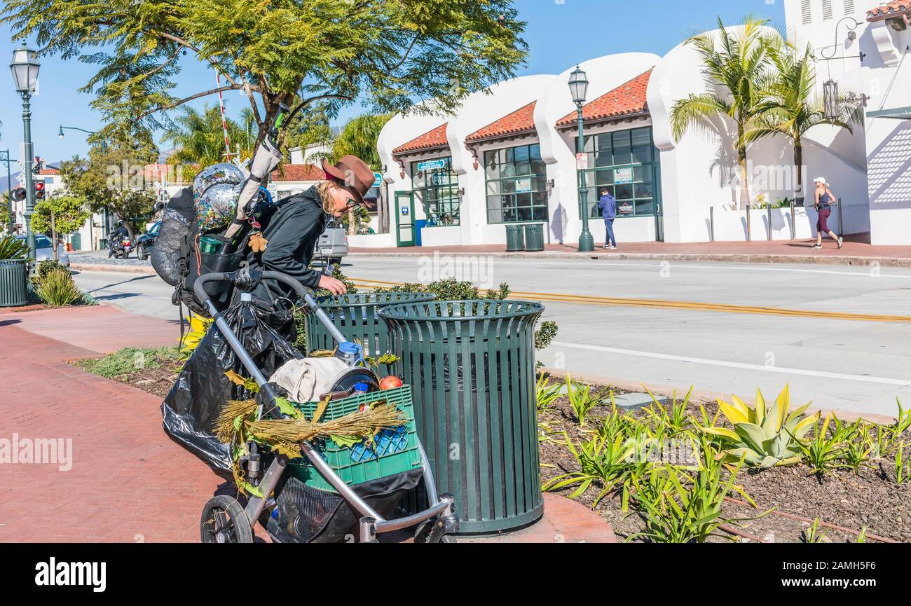 Frauen, die nach draußen gehen und mit einem Kinderwagen unterwegs sind, um ihre Besitztümer abzulegen, während sie auf der Suche nach Flaschen und Dosen in einem Mülleimer in der Stadt auf Santa Barbara sind. Stockfoto