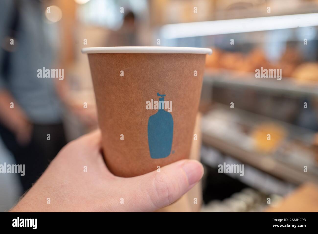 Einen Mann holding Einweg Kaffeebecher mit Logo auf der neu eröffneten blaue Flasche Kaffee Cafe auf der Santana Row Shopping Mall im Silicon Valley, San Jose, Kalifornien, 12. Dezember 2019. () Stockfoto