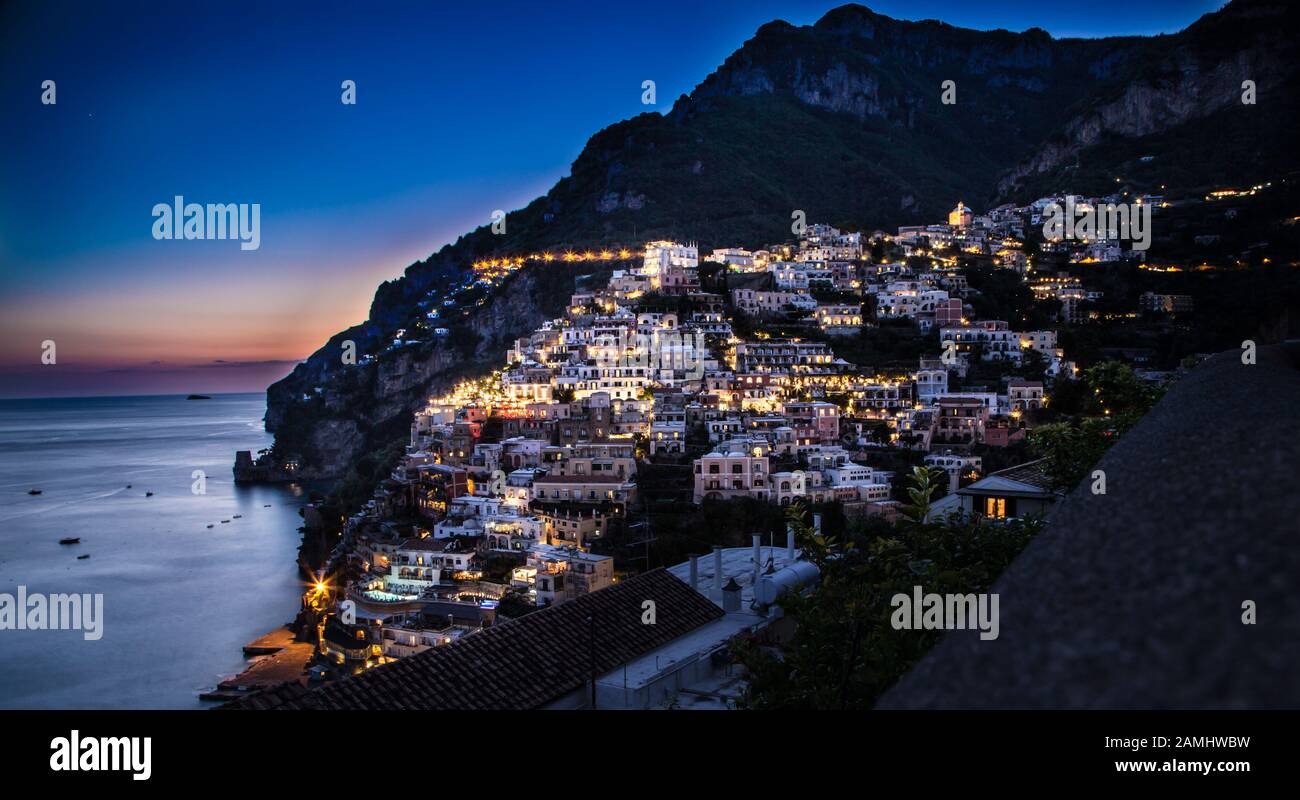 Auf der Suche über die Amalfi Küste bei Sonnenuntergang auf einen herrlichen Sommer Abend. Reichen warmen Farben Palette. Breite Slow Shutter. Flare von der Straße Leuchten unten. Stockfoto