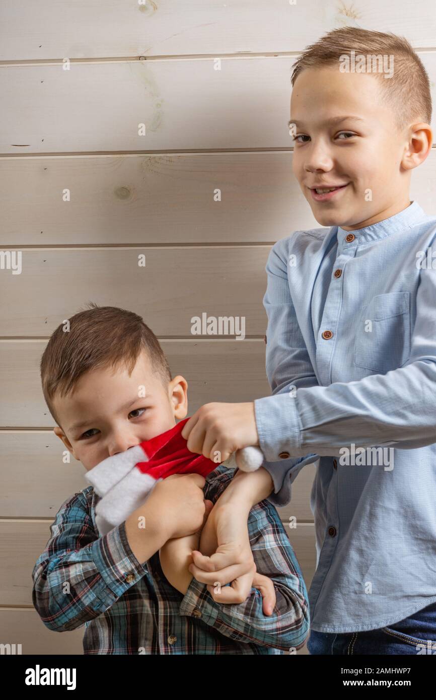 Ein 4-jähriger Junge in einem blauen Klepy-Hemd schreit auf hellem Holzhintergrund und sein 10-jähriger Bruder steht Stockfoto