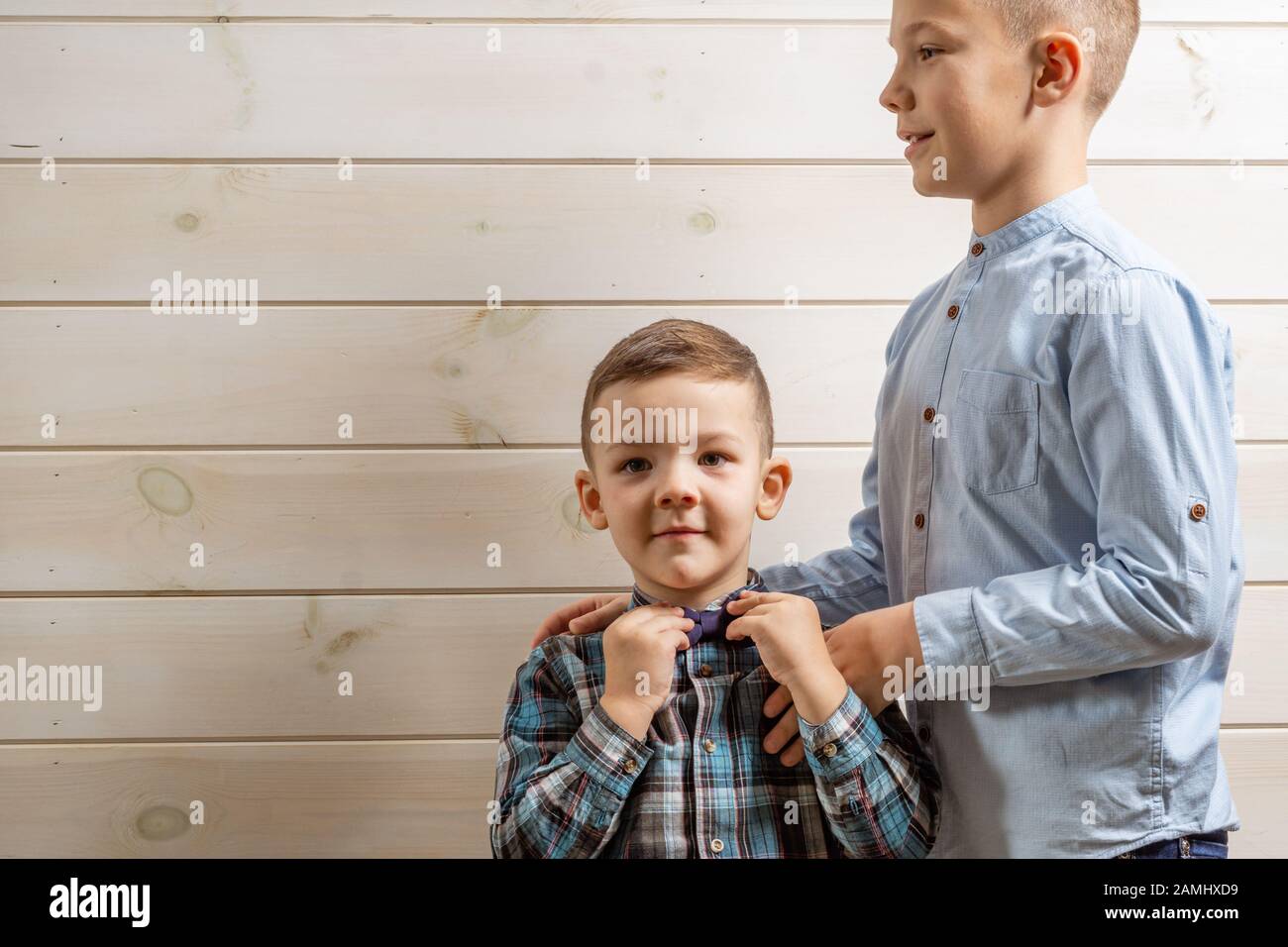 Ein 4-jähriger Junge in einem blauen Klepy-Hemd schreit auf hellem Holzhintergrund und sein 10-jähriger Bruder steht Stockfoto