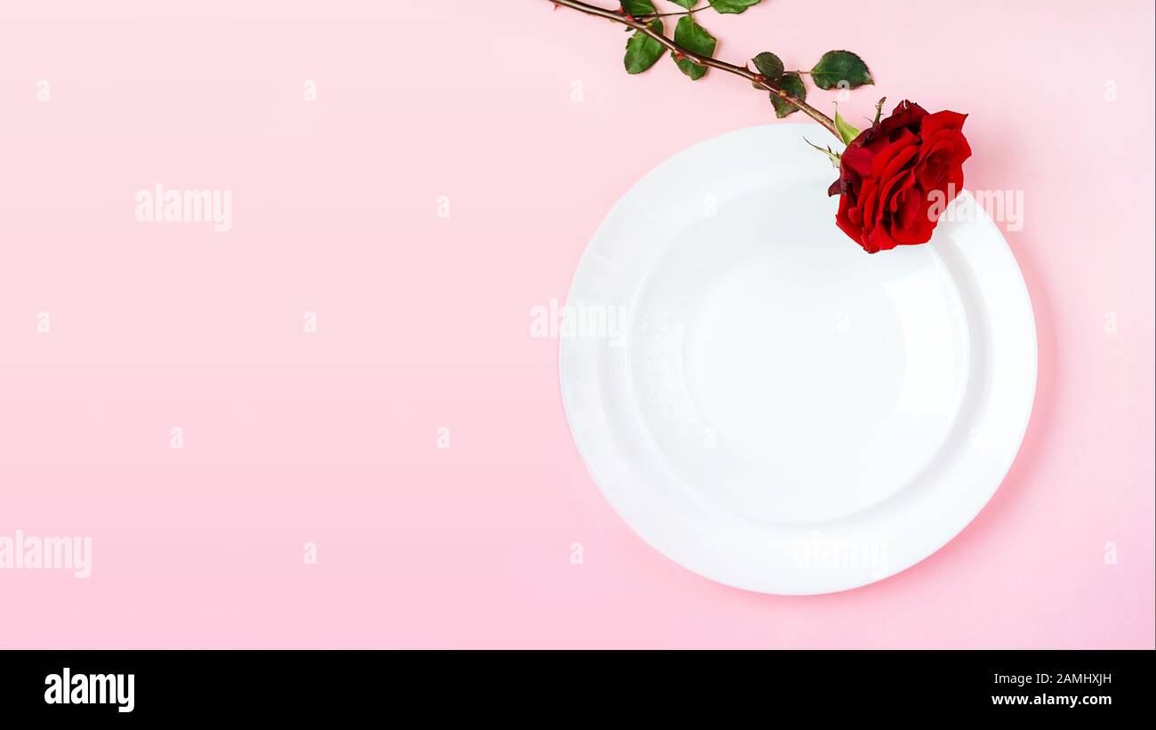 Romantisch gedeckten Tisch für Valentines Tag oder Abendessen Datum Feier Hochzeit. Valentines Tag Konzept mit rote Rose Bud White Platten auf Pastell rosa Tischdecke Hintergrund. Flach, Ansicht von oben kopieren. Stockfoto
