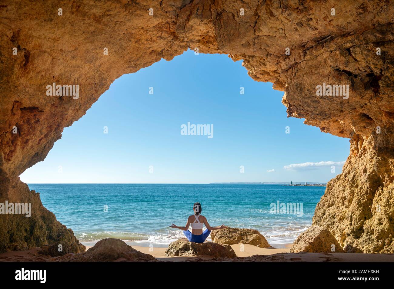 Frau, die in einer Höhle auf einem Felsen sitzt und Yoga am Meer praktiziert. Stockfoto