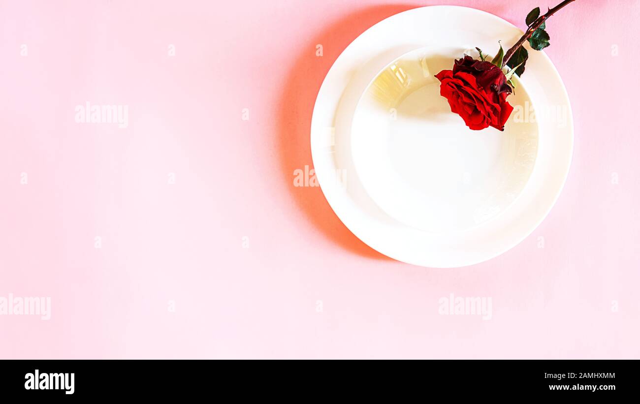 Romantisch gedeckten Tisch für Valentines Tag oder Abendessen Datum Feier Hochzeit. Valentines Tag Konzept mit rote Rose Bud White Platten auf Pastell rosa Tischdecke Hintergrund. Flach, Ansicht von oben kopieren. Stockfoto