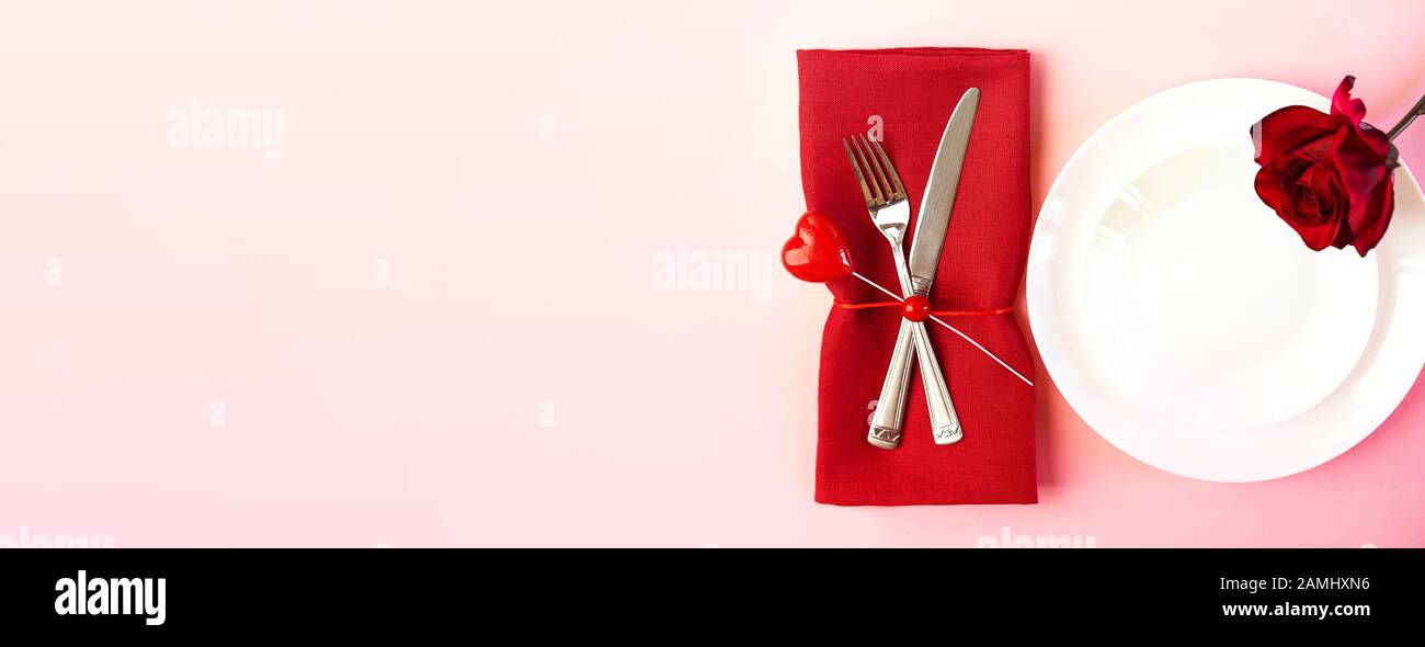 Romantisch gedeckten Tisch für Valentines Tag oder Abendessen Datum Feier Hochzeit. Valentines Tag Konzept mit rote Rose Bud White Platten auf Pastell rosa Tischdecke Hintergrund. Flach, Ansicht von oben kopieren. Stockfoto