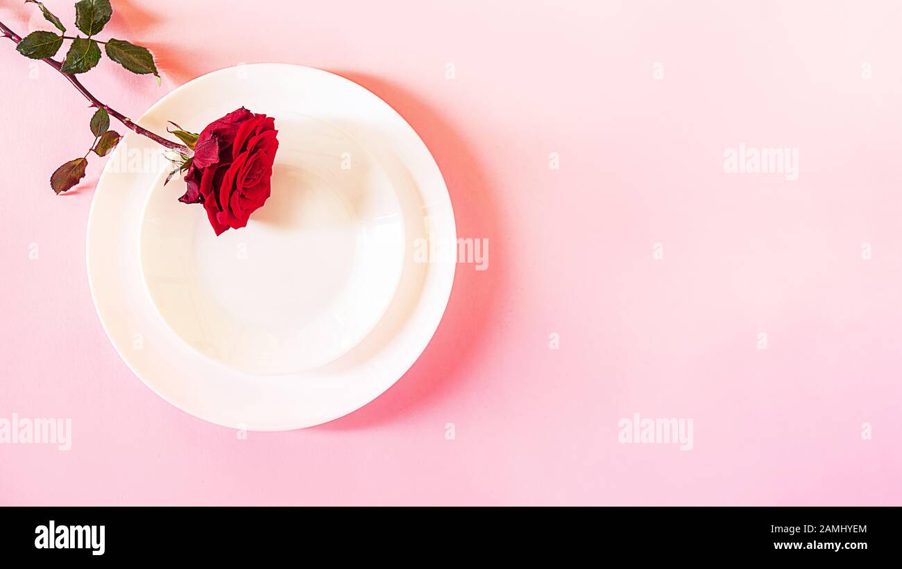Romantisch gedeckten Tisch für Valentines Tag oder Abendessen Datum Feier Hochzeit. Valentines Tag Konzept mit rote Rose Bud White Platten auf Pastell rosa Tischdecke Hintergrund. Flach, Ansicht von oben kopieren. Stockfoto