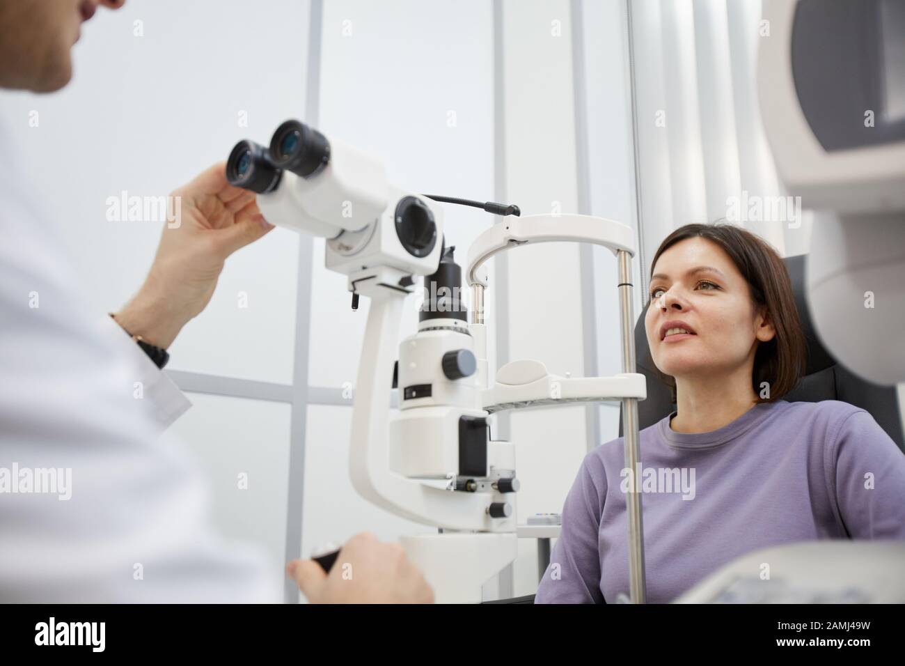 Porträt der jungen Frau, die sich während des Sehtests in der modernen Opthalmologie-Klinik mit dem Refraktometergerät beschäftigt, Kopierraum Stockfoto