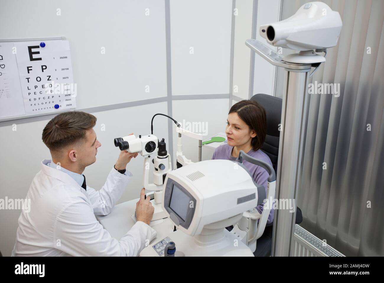 Hochwinkel-Porträt des männlichen Augenarztes mit ophtalmischem Refraktometer bei Rücksprache mit der weiblichen Patientin in der Klinik, Kopierraum Stockfoto