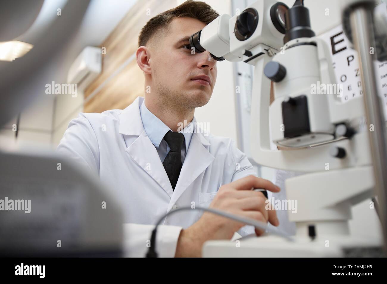 Das niedrige Winkelporträt des männlichen Optometristen mit Refraktometergerät, während die Sicht auf nicht erkennbare Patienten getestet wird Stockfoto