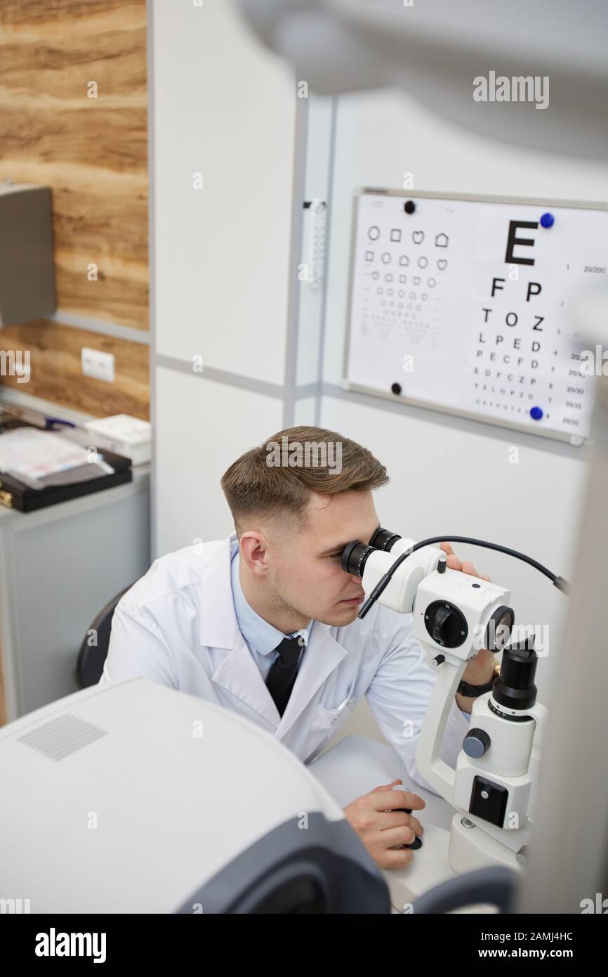 Hochwinkel-Porträt des männlichen Optometristen mit Refraktometergerät beim Testen der Sicht auf nicht erkennbare Patienten Stockfoto
