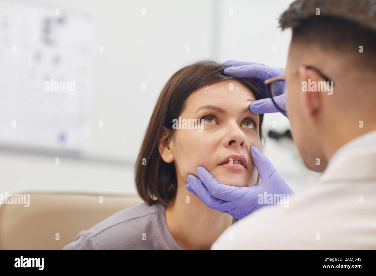 Rückansicht Portrait der jungen Augenärztin, die das Auge der weiblichen Patientin öffnet, während sie ihre Sehkraft in der medizinischen Klinik überprüft, kopiere Raum Stockfoto