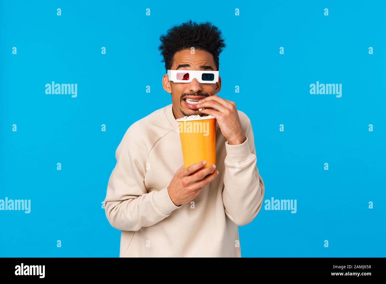 So ängstlich, aber interessant. Enertained hat einen lustigen afroamerikanischen Kerl gesehen, der Horrorfilm im Kino sieht, Popcorn und einen mit Kränzchen aussehenden Bildschirm isst Stockfoto