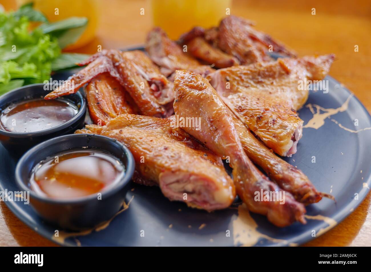 Gegrilltes Huhn im thailändischen Stil auf schwarzem Keramikgericht mit Sriracha und süßer Soße. Stockfoto
