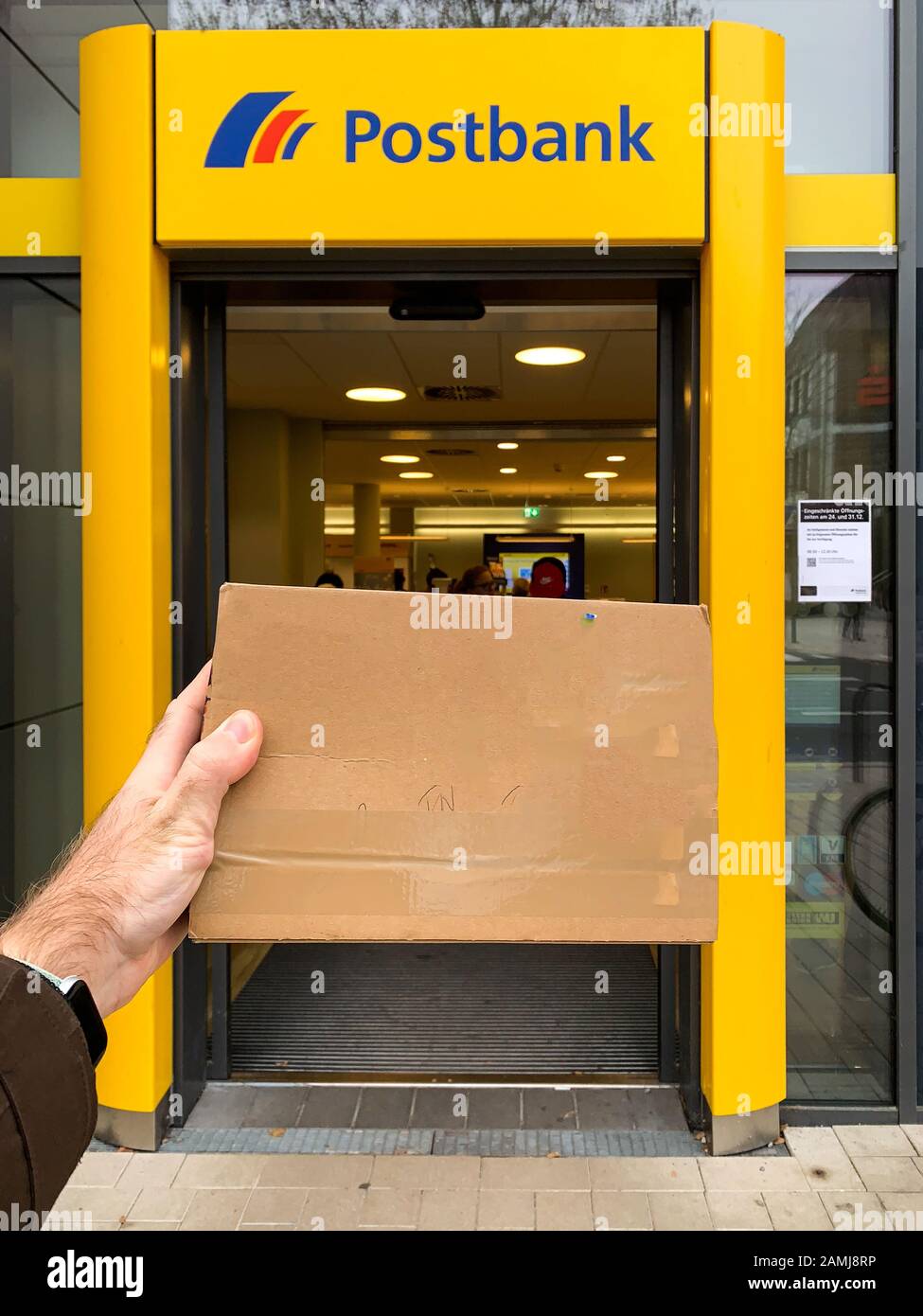 Frankfurt, Deutschland - 27. Dezember 2019: Man Hand hält Briefumschlag vor Postbank Postamt in deutscher POV-Perspektive Stockfoto