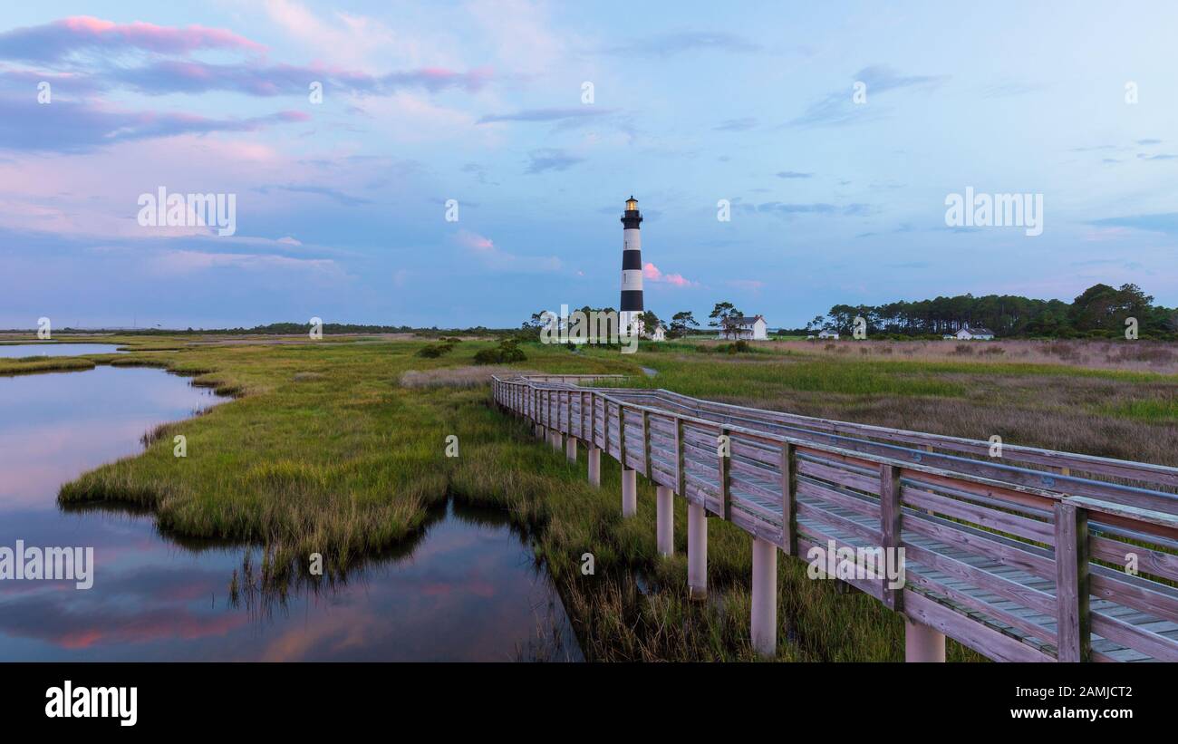 Sonnenuntergang am Bodie Island Lighthouse in den Outer Banks, North Carolina, mit Holzsteg im Vordergrund über Ozeanmarschen Stockfoto