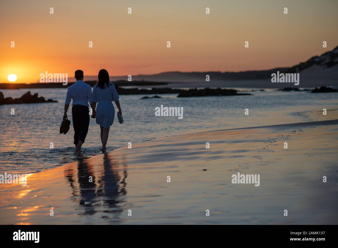 Ein Paar, das bei Sonnenuntergang am Strand spazieren geht Stockfoto