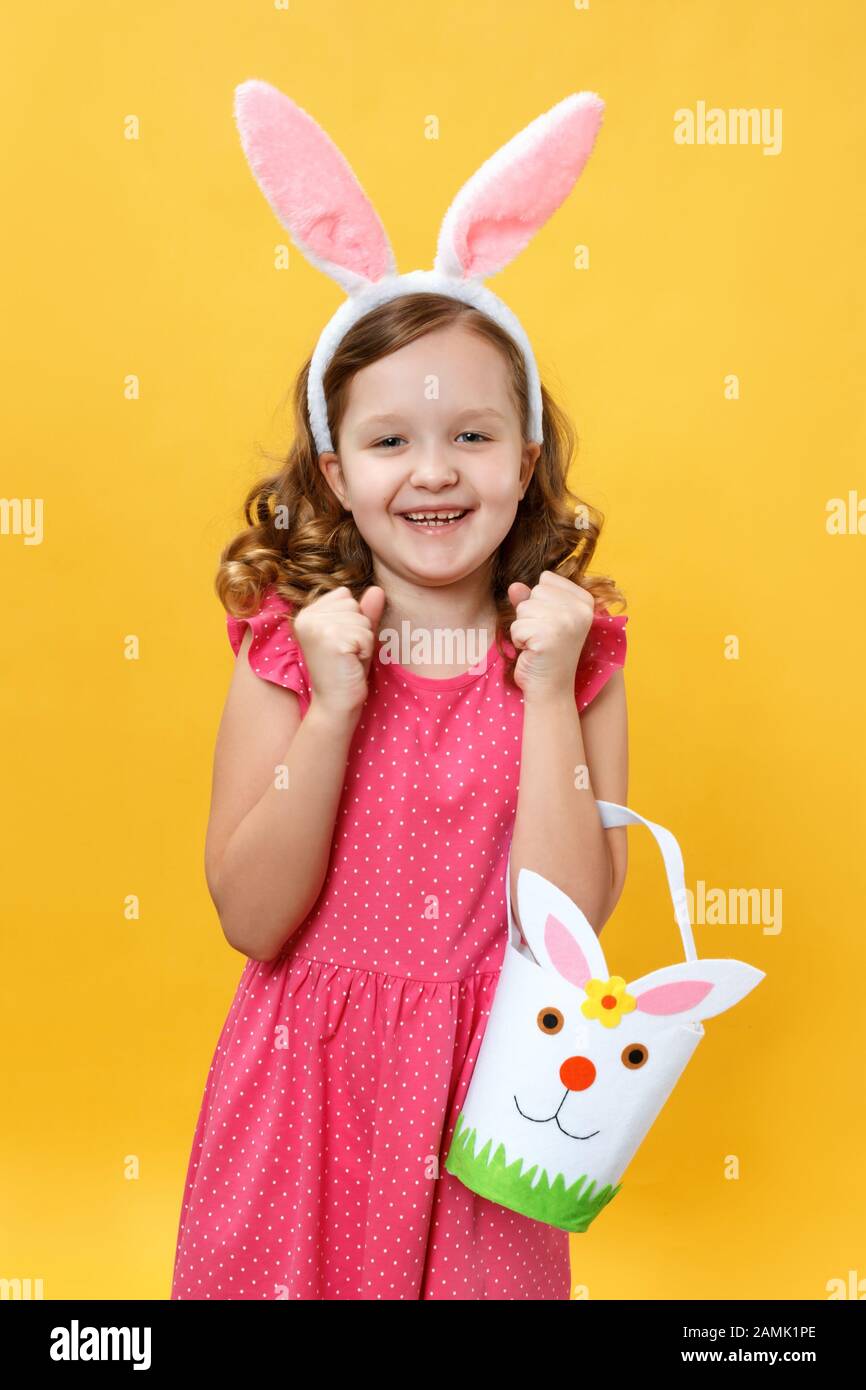 Osterkonzept. Ein fröhliches kleines Mädchen in den Ohren eines Hunnys hält  einen Beutel für Süßigkeiten und Eier. Porträt eines freudigen Kindes auf  gelbem Hintergrund Stockfotografie - Alamy