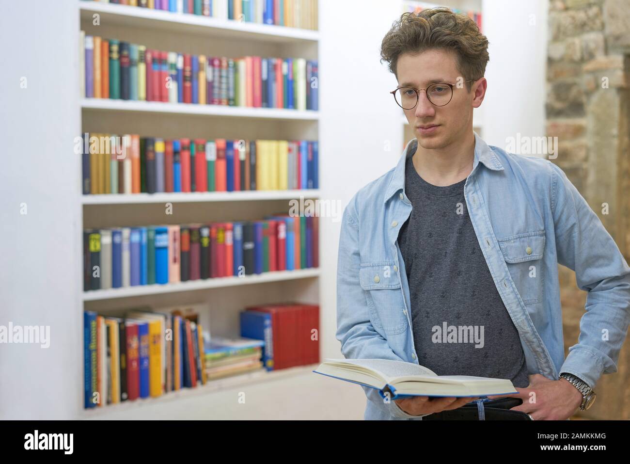 Nachdenklicher junger Student in einer Hausbibliothek denkt über das Buch nach, das er in der Universität liest. Stockfoto