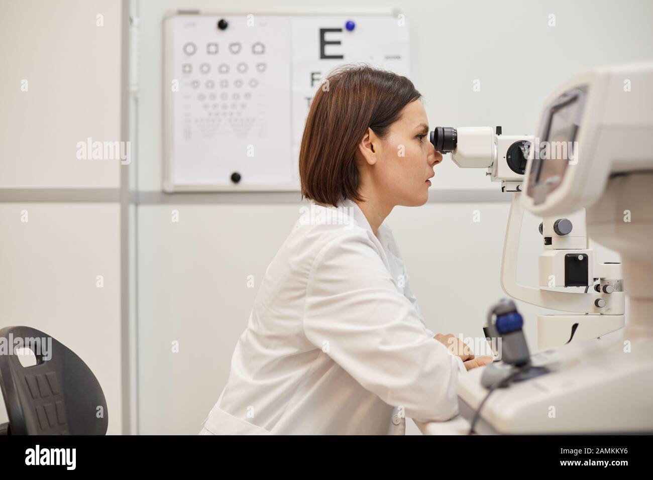Seitenansicht Porträt junger Augenärztin mit Refraktometergerät während des Sehtests in der modernen Klinik, Kopierraum Stockfoto
