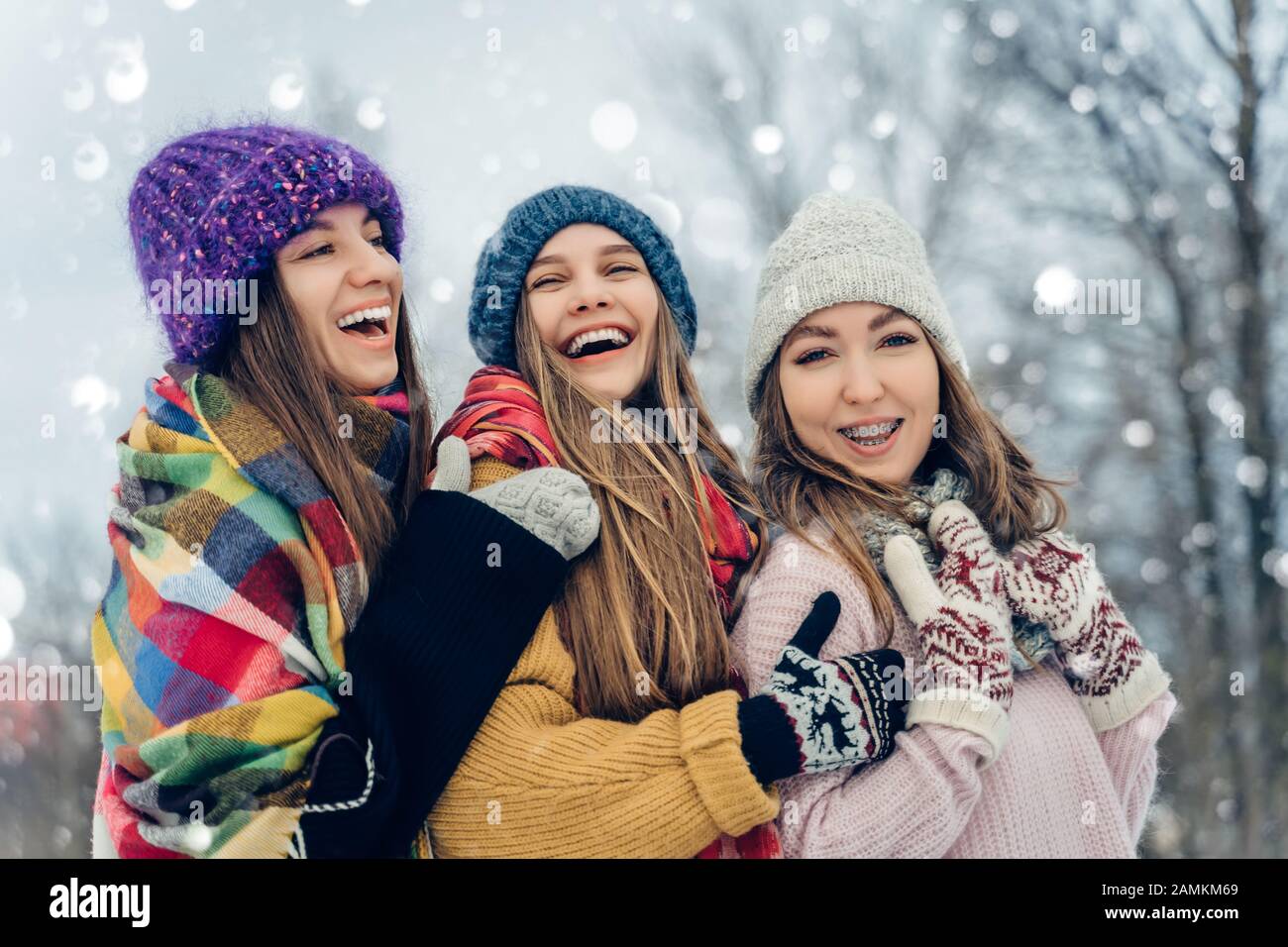 Drei Frauen Freunden sich im Freien in Strickmützen an, die bei schneebedecktem Wetter Spaß haben. Gruppe junger weiblicher Freunde im Winter im Freien. Stockfoto