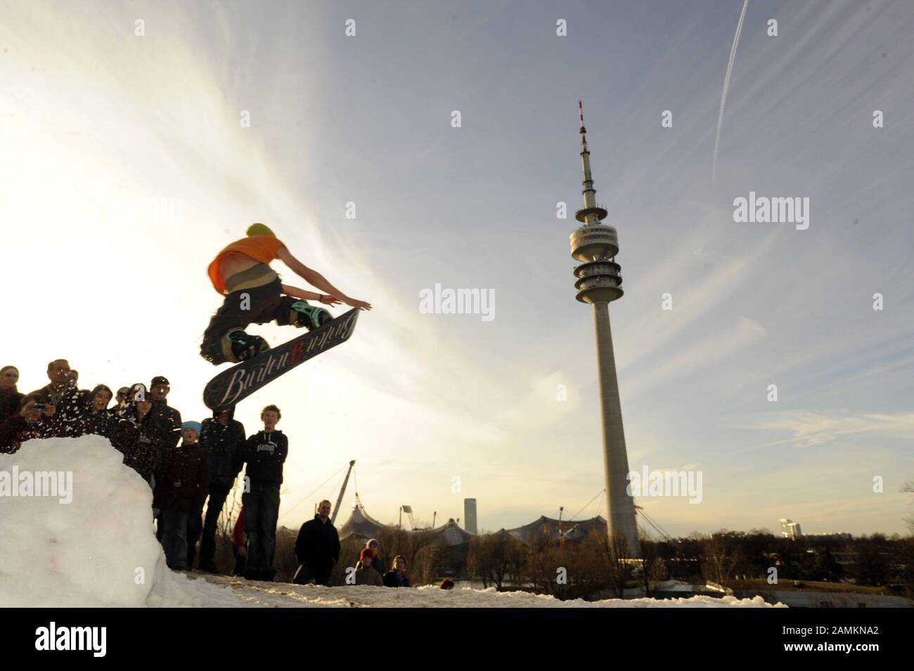 Freistil-Snowboarder beim Abstieg vom Olympia-Berg beim Wintersportfest im Münchner Olympiapark mit dem Olympiaturm im Hintergrund. [Automatisierte Übersetzung] Stockfoto