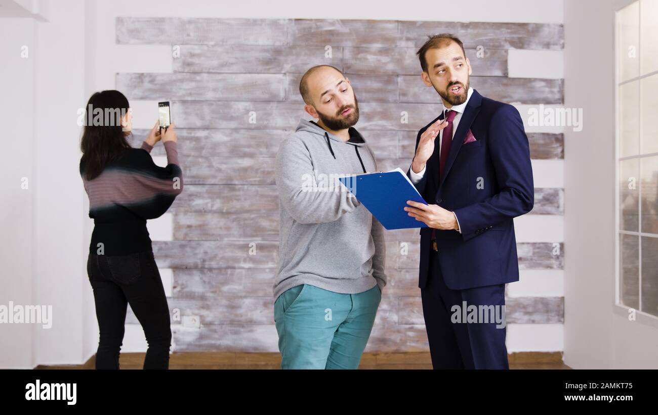 Immobilienmakler im Gespräch mit dem Kunden in leerer Wohnung. Frau fotografiert in leerer Wohnung. Stockfoto