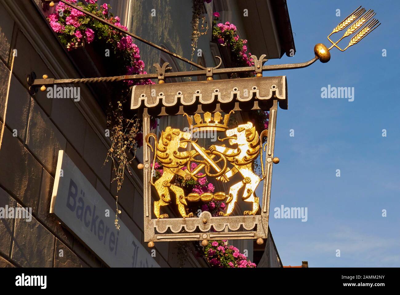 Goldenes Zunfzeichen einer Bäckerei in Bad Tölz, Krone, Löwen mit gekreuzten Schwertern und Brezel sowie drei Rollen, Balkone mit Blumenkästen, 12.10...2014, [automatisierte Übersetzung] Stockfoto