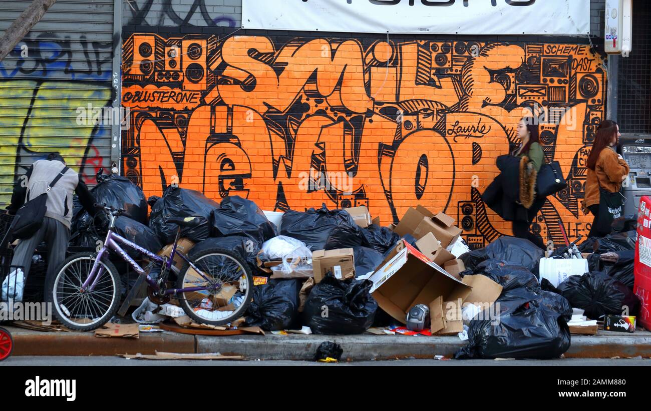 Die Leute laufen an einem Müllhaufen auf einem Bürgersteig in New York City vorbei, mit Graffitis im Hintergrund und jemand, der durch den Müll wühlt, 12. Januar 2020. Stockfoto