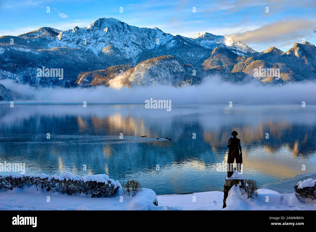 Herzogstand 1.731 m mit Kochelsee, frühmorgens, teils Nebel, Schnee auf dem Gipfel, vor der Skulptur Fischerjung - Fischer vom Kochelsee, die erstmals 1952 aus einer Drahtkonstruktion mit Putz und Ton errichtet wurde, die vom Bildhauer Prof. Richard Miller geschaffen wurde, Renoviert und vor einigen Jahren von Oswald Rifesser aus St. Ulrich in Tyrol, 10.01.2017 [automatisierte Übersetzung] Stockfoto