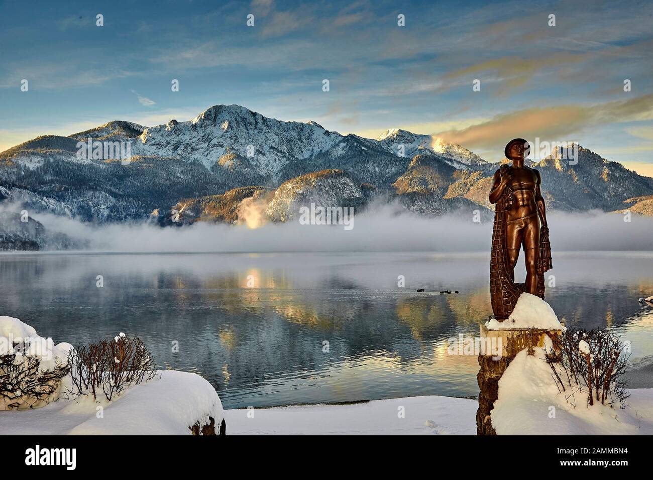 Herzogstand 1.731 m mit Kochelsee, frühmorgens, teils Nebel, Schnee auf dem Gipfel, vor der Skulptur Fischerjung - Fischer vom Kochelsee, die erstmals 1952 aus einer Drahtkonstruktion mit Putz und Ton errichtet wurde, die vom Bildhauer Prof. Richard Miller geschaffen wurde, Renoviert und vor einigen Jahren von Oswald Rifesser aus St. Ulrich in Tyrol, 10.01.2017 [automatisierte Übersetzung] Stockfoto