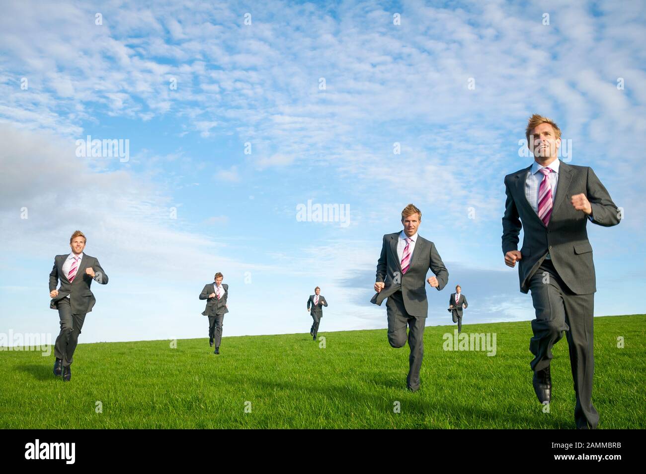 Team von geklonten Geschäftsleute vorwärts laufen draußen im grünen Gras Wiese unter strahlend blauem Himmel Stockfoto