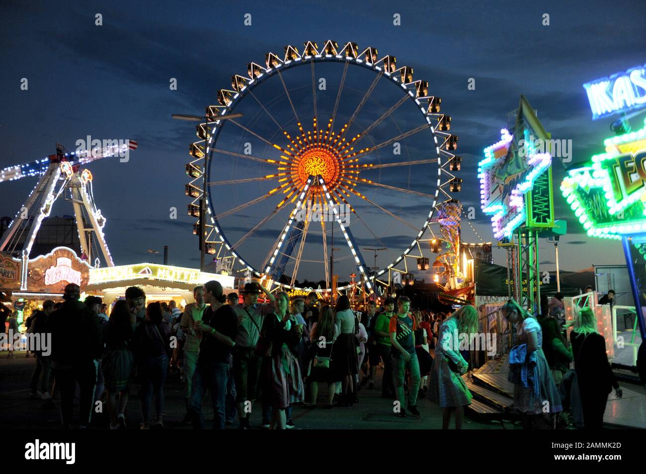 Oktoberfestbesucher vor hell erleuchteten Fahrten auf der nächtlichen Wiesn. [Automatisierte Übersetzung] Stockfoto