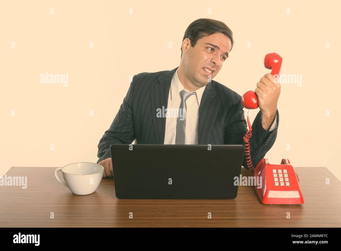 Betonte, dass der persische Geschäftsmann mit einem alten Telefon spricht, während er einen Laptop bei der Arbeit verwendet Stockfoto
