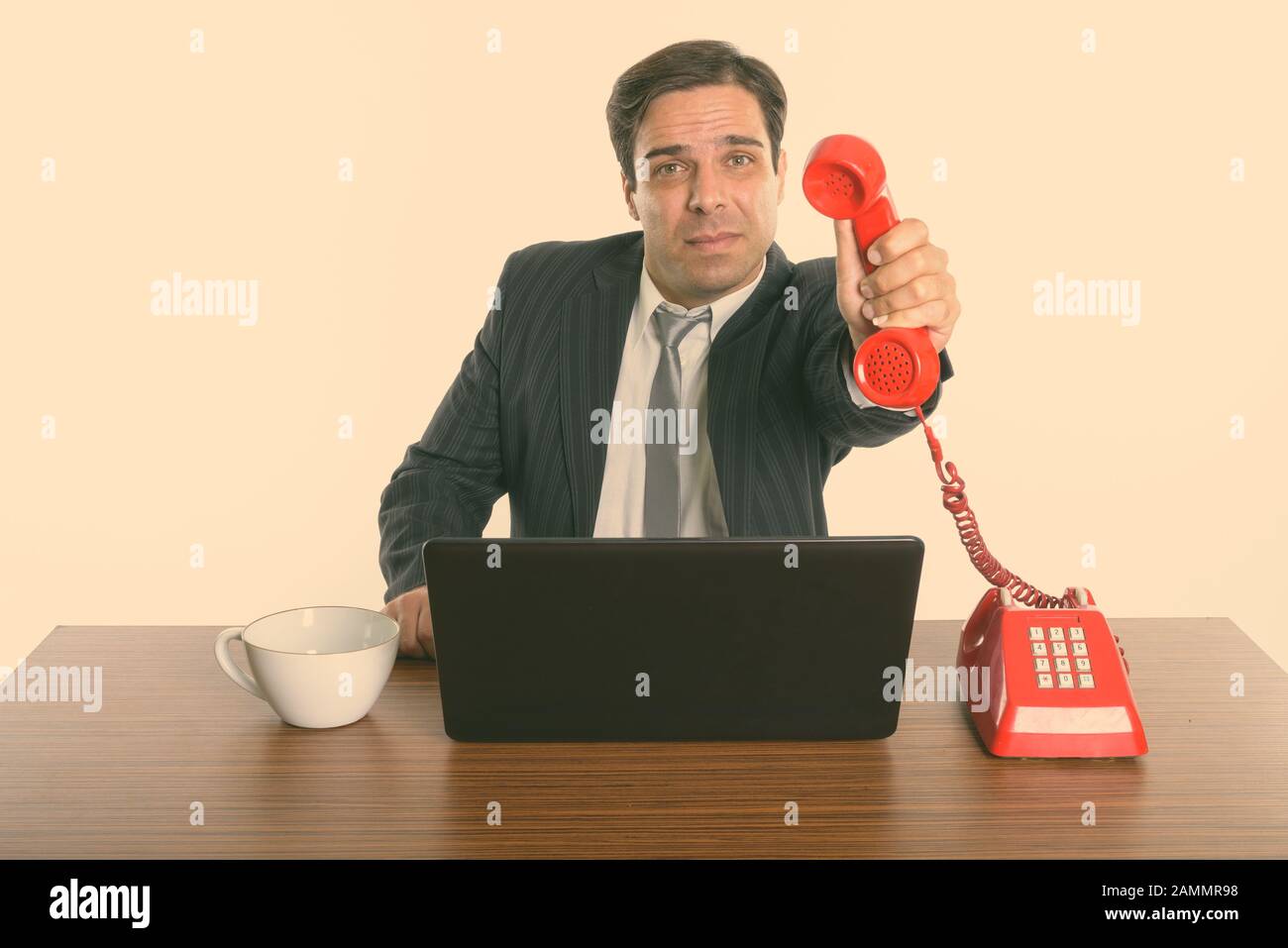 Persischer Geschäftsmann, der bei der Arbeit ein altes Telefon gibt, während er einen Laptop verwendet Stockfoto
