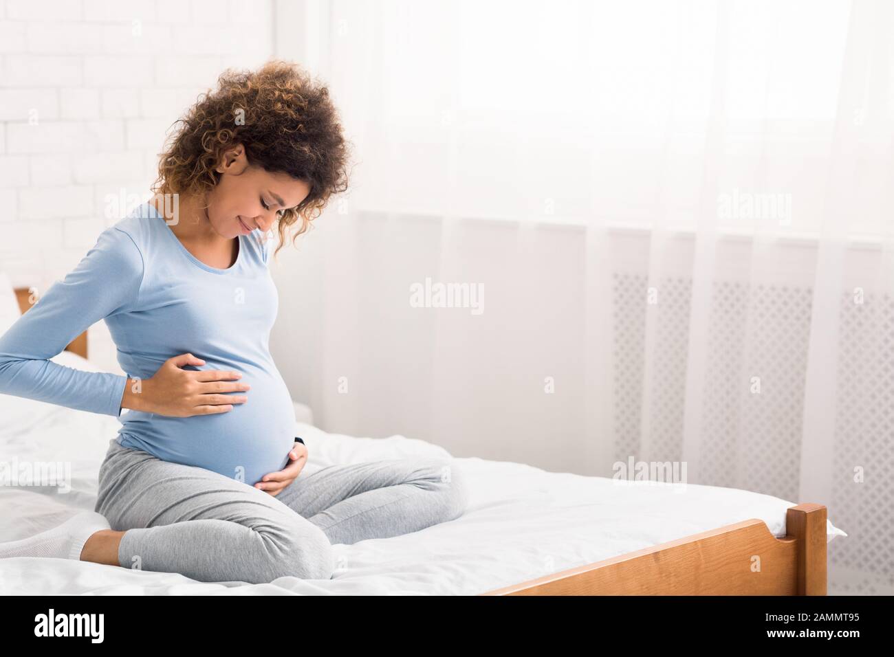 Ziemlich afro-schwangere Frau, die die Hände auf dem Bauch hält Stockfoto