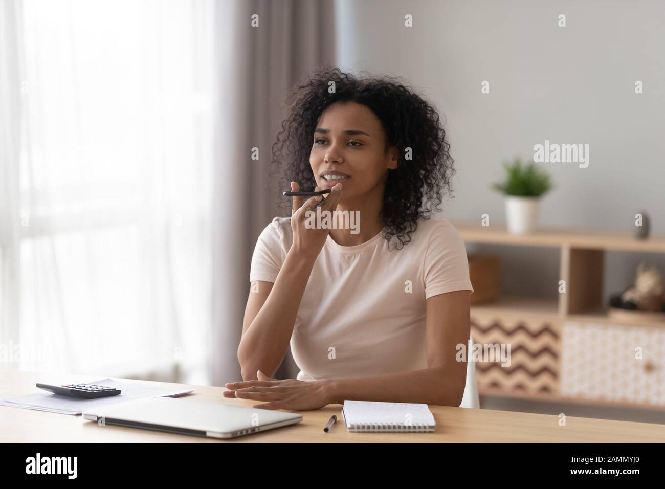 Afrikanische Frau sitzt am Schreibtisch und hält die Sprachnachricht des Smartphones Stockfoto