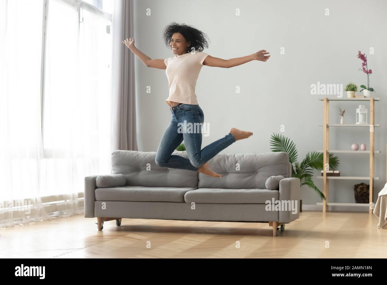 Fröhliche afrikanerin in Luft im Sprung ins Wohnzimmer Stockfoto