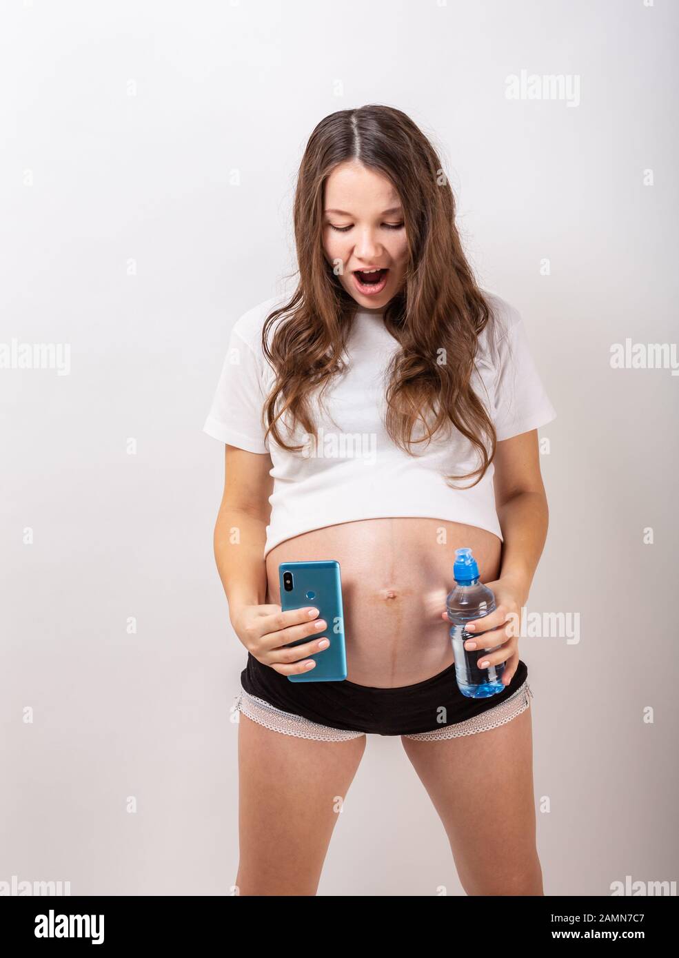 Schöne schwangere brünette Frau trinkt Wasser aus der Flasche auf isoliert weißer Hintergrund Stockfoto