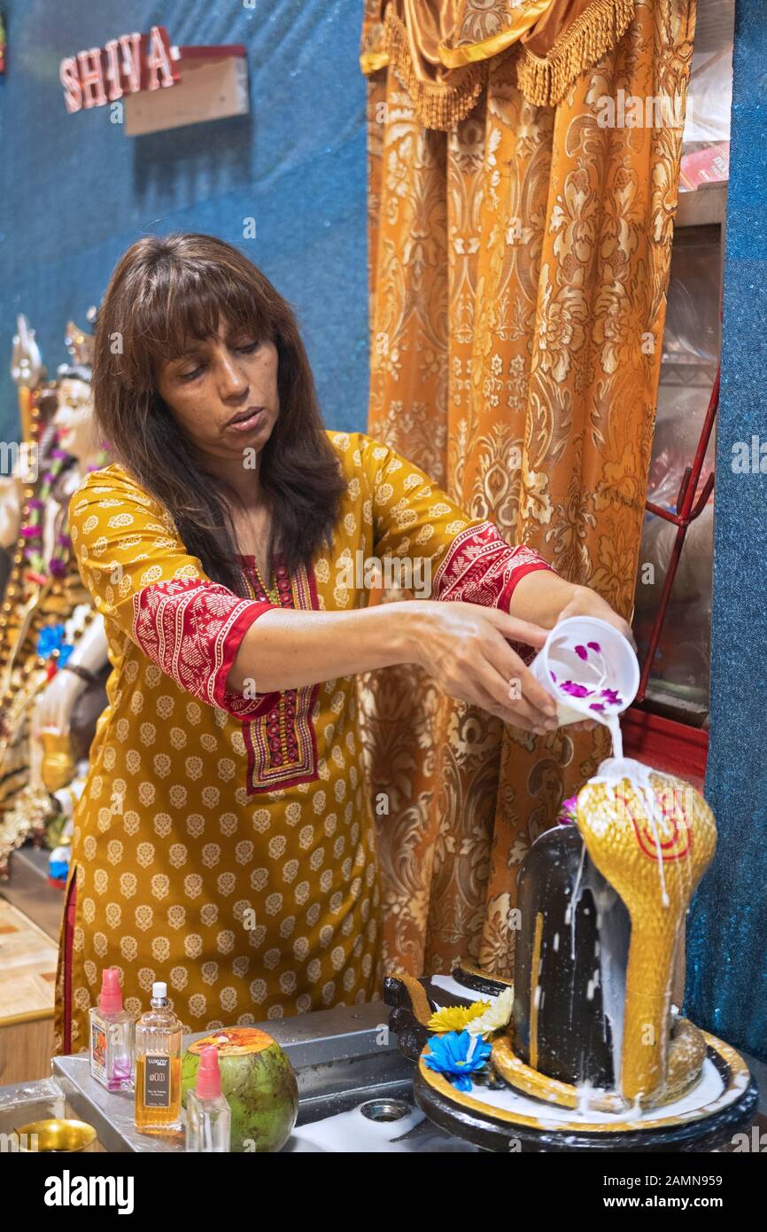 Eine Hindu-Frau in einer Sari gießt Milch über einen Shiva-Lingam in einem Tempel in Jamaika, Queens, New York City. Stockfoto