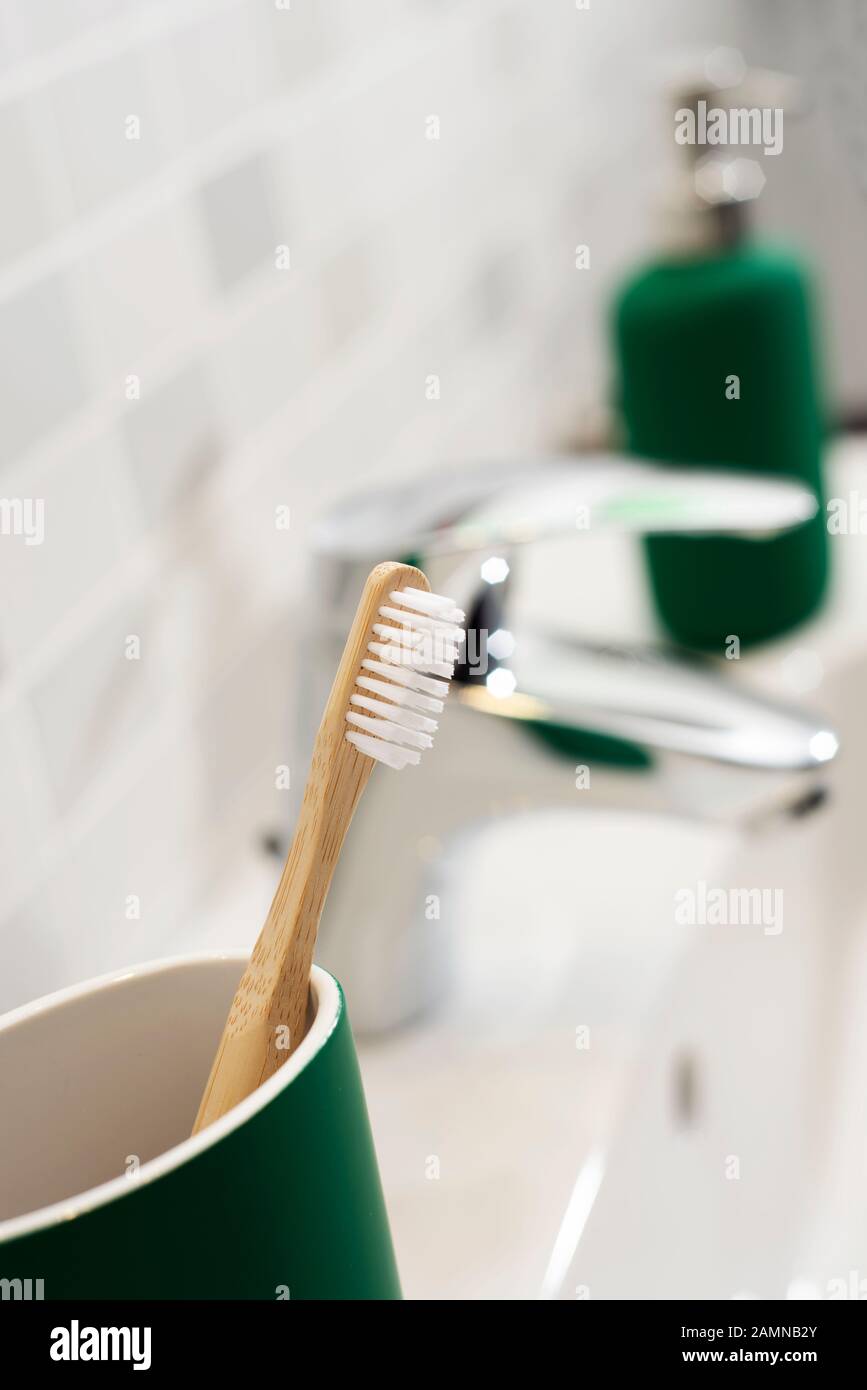 Nahaufnahme einer Bambuszahnbürste in einem grünen Zahnbürstentopf neben dem Waschbecken eines Badezimmers Stockfoto