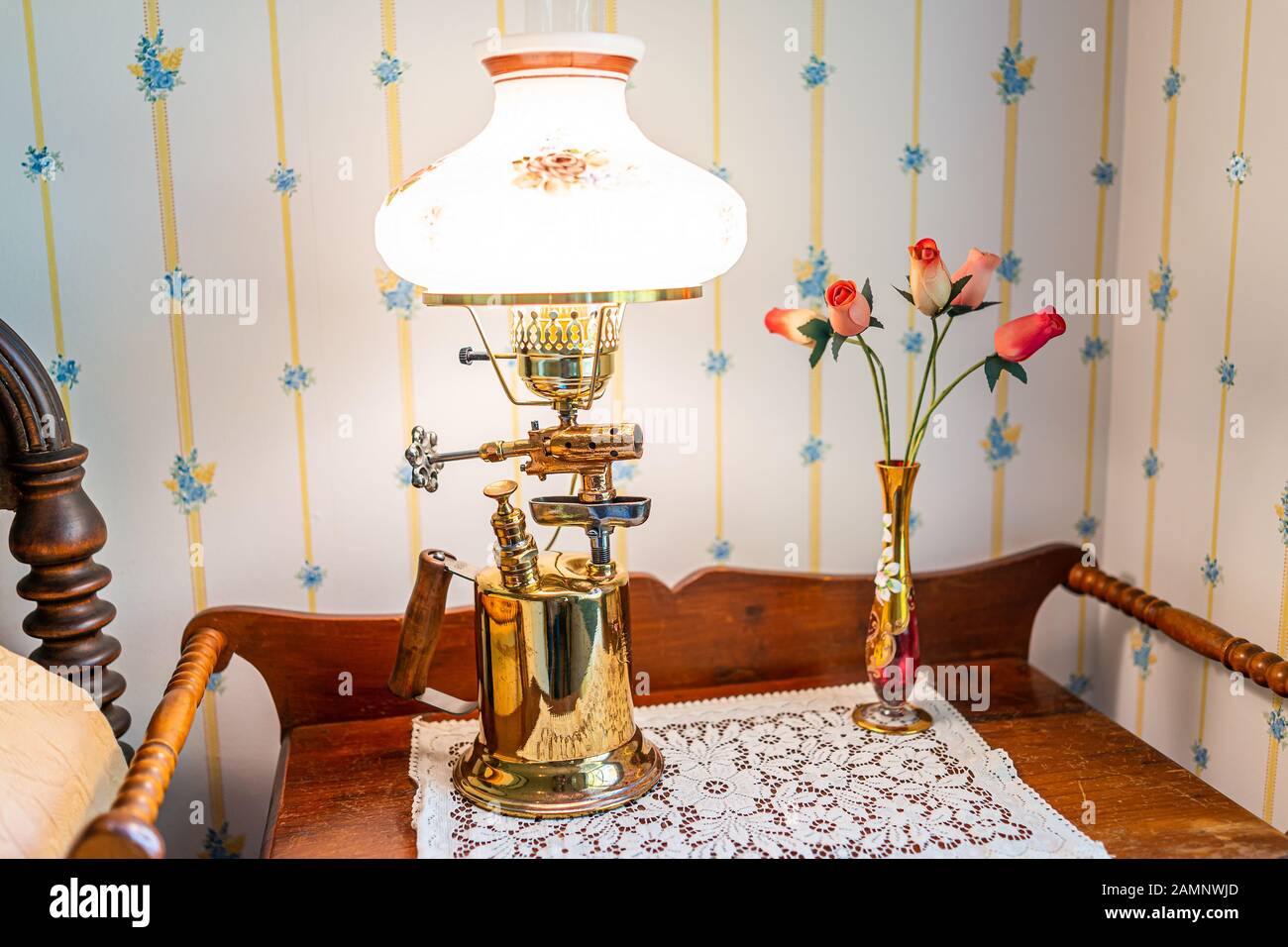 Nachttisch am Bett mit alter Retro-Lampe im Schlafzimmer des Hauses mit  hellem Licht und Blumen in Vase an der Tapetenwand Stockfotografie - Alamy
