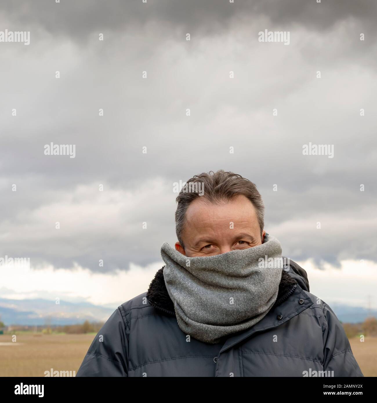 Kaukasischer Mann mit Wollschal bedeckt, um sich vor der Kälte zu schützen, mit trübem Himmel im Hintergrund Stockfoto