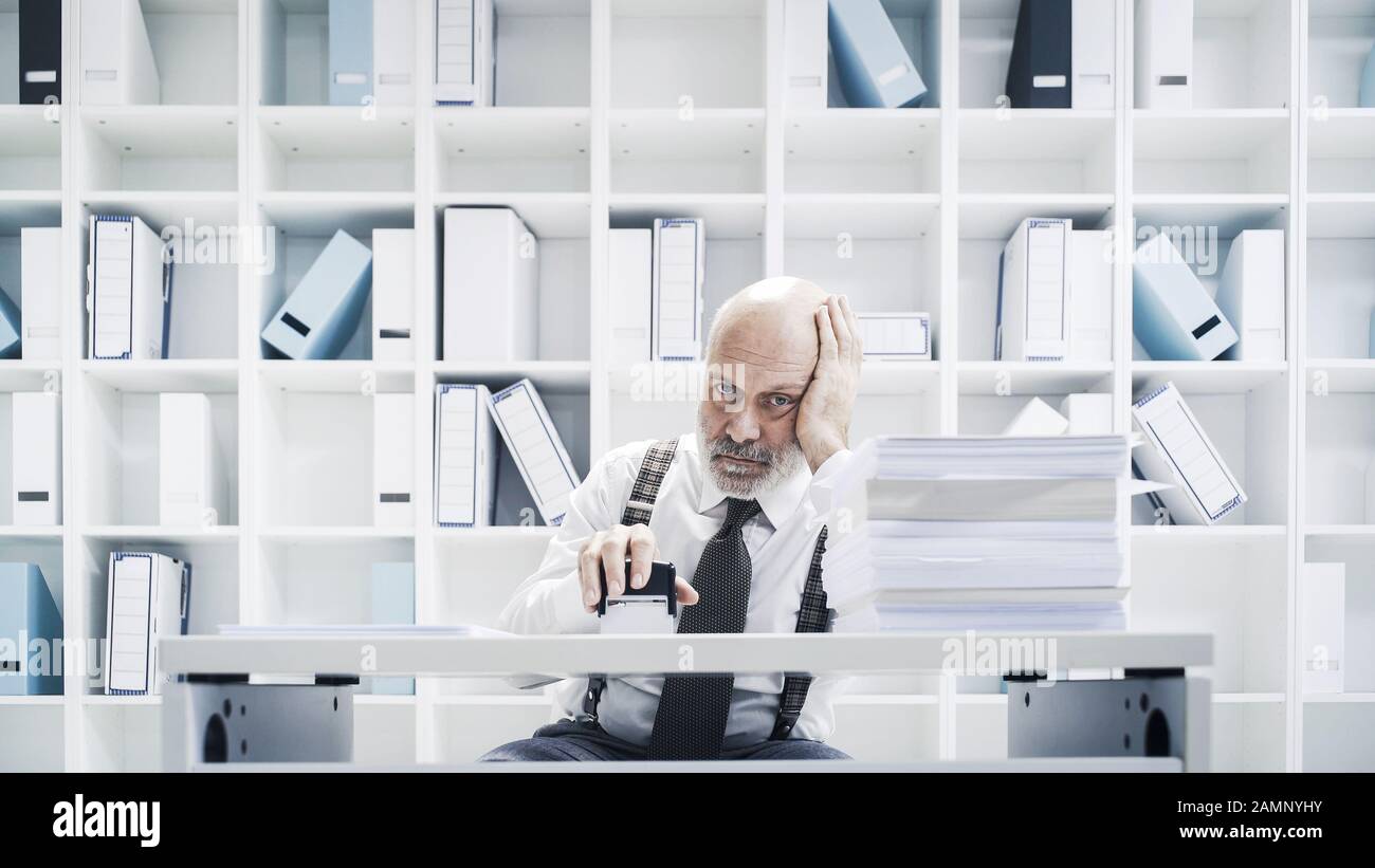 Leitender Angestellter der Unternehmensleitung, der im Büro eine langweilige Arbeit macht, stempelt er Papierkram Stockfoto
