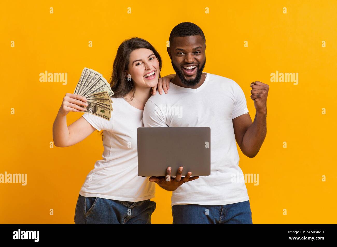 Überfreutes interracial Paar mit Dollar-Bargeld und Laptop feiern Gewinn zusammen Stockfoto