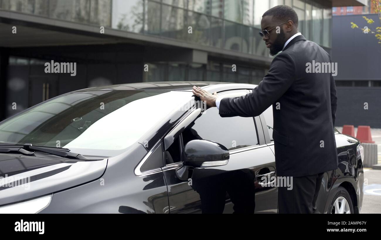 Der skrupellose afro-amerikanische Mann wischt sein neues Auto, bevor er den Parkplatz verlässt Stockfoto