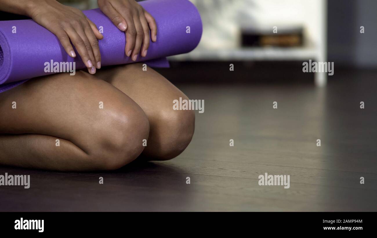 Junge Frauen sitzen auf dem Boden mit gerollter Yogamatte, körperliches Training im Fitnessstudio Stockfoto