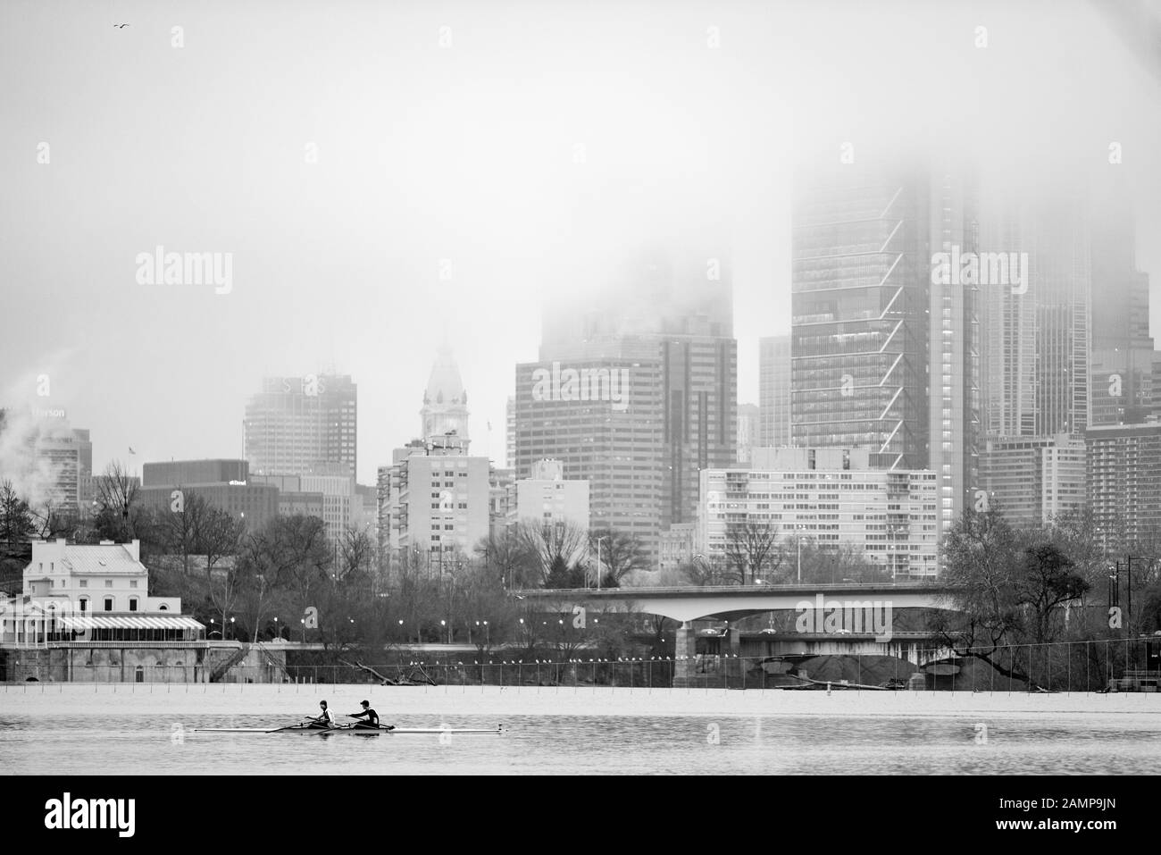 Ein Schwarz-Weiß-Bild von zwei Ruderern in einer Möwe vor einem nebelbedeckten Stadtbild. Stockfoto