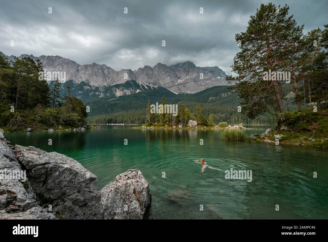 Frau schwimmt im See, Felsen am Ufer, Blick in die Ferne, Eibsee vor Zugspitzmassiv mit Zugspitze, Wetterstein Range Stockfoto